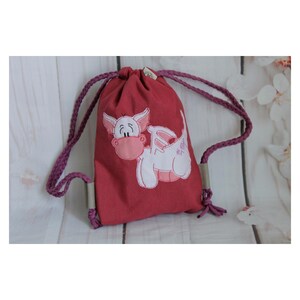 Könnte beinhalten: Rote Kordeltasche mit einem weißen gestickten Drachen mit rosa Akzenten. Der Drache hat eine rosa Nase und rosa Flügel.