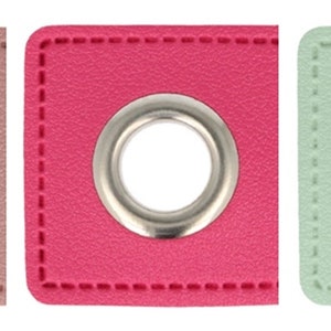 Può includere: Tre toppe quadrate di tessuto con un occhiello metallico al centro. Le toppe sono rosa, rosso e verde chiaro.