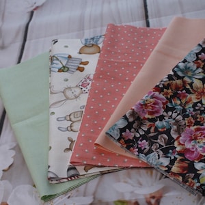 May include: Five different fabric swatches, including a green, a white with a bunny and bear print, a pink with white polka dots, a peach, and a black with floral print.