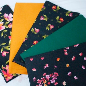Può includere: Cinque campioni di tessuto, due con sfondo nero e motivi floreali, uno giallo senape tinta unita e due colori tinta unita, uno verde scuro e uno nero.
