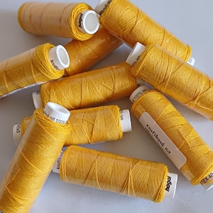 May include: A close-up of a pile of yellow thread spools. The spools are labelled "Knoflíková nit" and "hagal".