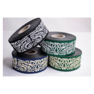 May include: Four spools of woven ribbon featuring an intricate repeating knotwork pattern. The collection includes a black spool with silver embroidery, a green spool with white embroidery, a blue spool with cream embroidery, and a green spool with cream embroidery.