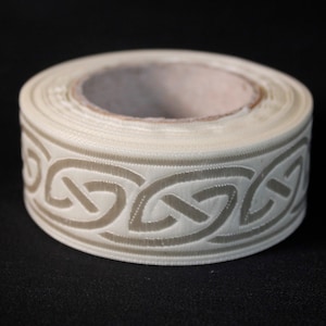 May include: A roll of white satin ribbon with a raised, embossed Celtic knot design in a light brown color.
