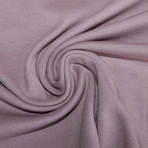 Könnte beinhalten: Nahaufnahme eines weichen, mauvefarbenen Stoffes mit einer glatten, leicht strukturierten Oberfläche. Der Stoff ist gefaltet und drapiert und erzeugt einen sanften, fließenden Effekt.