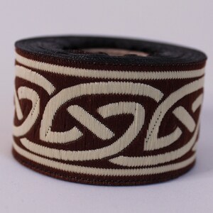May include: Brown and cream trim with a Celtic knot design. The trim is rolled up on a spool.