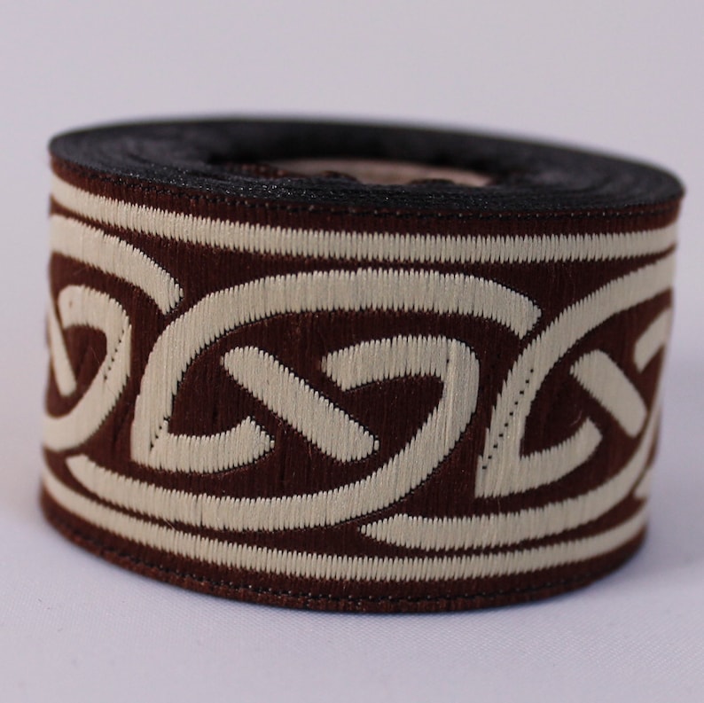 May include: Brown and cream trim with a Celtic knot design. The trim is rolled up on a spool.