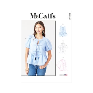 Könnte beinhalten: Eine Frau trägt ein hellblaues, gestreiftes Oberteil mit Schleifen und kurzen Puffärmeln. Dazu eine blaue Jeans. Das Bild zeigt auch ein Schnittmuster mit dem McCall's-Logo und der Nummer M8557.