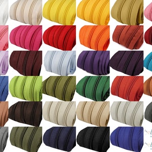 Könnte beinhalten: Sortiment von 24 Reißverschlussbändern in verschiedenen Farben, darunter Weiß, Rosa, Rot, Hellblau, Lavendel, Grün, Braun, Beige, Grau, Schwarz und Blau. Jedes Reißverschlussband ist etwa 1 Zoll breit.