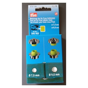 Könnte beinhalten: Eine blaue und weiße Verpackung für ein Prym Werkzeug-Set für Hohlnieten. Die Box zeigt eine Nahaufnahme der Werkzeuge, die silberfarben sind mit grünen Gummieinsätzen. Die Box enthält auch den Text "Werkzeug-Set für Prym Hohlnieten", "Tool set for Prym tubular rivets", "Jeu d'outils pour rivets creux Prym", "Art.No.: 390 903", "Ø 7,5 mm", und "Ø 9,0 mm".