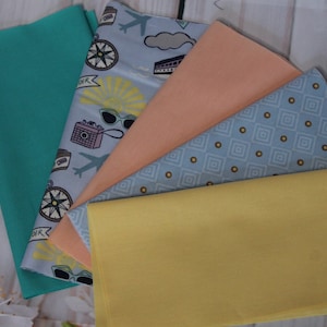 Könnte beinhalten: Eine Sammlung gefalteter Stoffe in verschiedenen Farben und Mustern. Enthält unifarbene Stoffe in Türkis, Pfirsich und Gelb sowie gemusterte Stoffe mit Reise-Designs und geometrischen Formen.