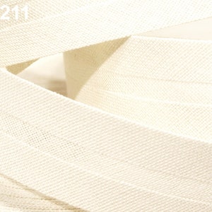 Könnte beinhalten: Nahaufnahme eines weißen Baumwollbandes mit einer strukturierten Webart. Das Band ist in der Mitte gefaltet und die Kanten sind sichtbar. Das Band ist 100211.