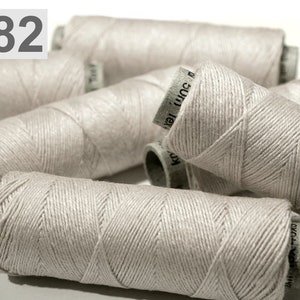 May include: A collection of light beige thread spools. The spools are cylindrical, with the thread meticulously wound. The number "882" is visible in the top left. The spools are arranged in a slightly overlapping pattern, suggesting a craft or sewing theme.
