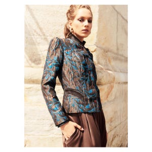 Könnte beinhalten: Gemusterte Jacke mit hohem Kragen und Knopfverschluss. Die Jacke hat eine braune und schwarze Basis mit blauen blattartigen Designs. Das Model trägt einen braunen Rock. Die Jacke hat lange Ärmel und eine taillierte Taille.