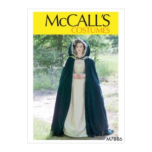 Könnte beinhalten: McCall's Costumes Schnittmuster M7886 für eine Kapuzencape aus grünem Samt. Das Model trägt ein weißes Kleid und eine grüne Samtcape mit Kapuze. Das Schnittmuster ist für Kostüme.