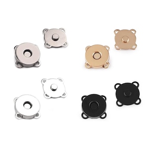 Op de afbeelding: Assortiment van magnetische drukknopen in zilver, goud en zwart. Elke sluiting heeft een ronde knop met een kleine metalen cirkel in het midden en vier pinnen die uit de knop steken.