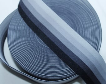 May include: A roll of grey and black elastic trim with a gradient effect. The trim is folded in half and the ends are overlapping.