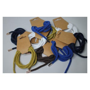 Pode incluir: Uma coleção de cadarços coloridos em várias tonalidades, incluindo azul, branco, marinho, castanho e dourado. Cada par é enrolado e preso a uma etiqueta de cartão castanho com um furo para exposição. Os cadarços têm ponteiras metálicas.