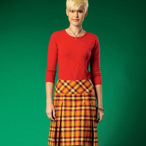 Könnte beinhalten: Eine Frau trägt einen roten Langarm-Pullover und einen gelben, orangefarbenen und schwarzen karierten Rock.