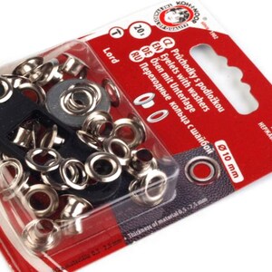 Può includere: Un pacchetto da 20 set di occhielli argentati con rondelle, ognuno con un diametro di 10 mm. La confezione è rossa e bianca con il testo "Eyelets with washers" e "Průchodky s podložkou" in più lingue.