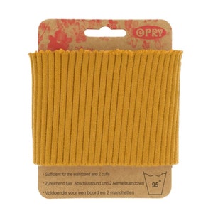 Könnte beinhalten: Eine Packung gerippter Strickware in Senfgelb. Die Packung ist mit "OPRY" gekennzeichnet und enthält Waschhinweise bei 95 Grad Celsius. Der Text auf der Packung lautet: "Sufficient for the waistband and 2 cuffs", "Zureichend fuer Abschlussbund und 2 Aermelbuendchen", und "Voldoende voor een boord en 2 manchetten".