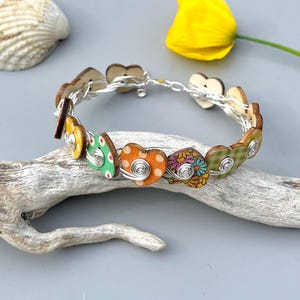 May include: A handmade bracelet featuring wooden heart-shaped beads. The beads are adorned with various patterns and colors, including polka dots and floral designs. The hearts are connected by silver wire, creating a unique and artistic accessory.