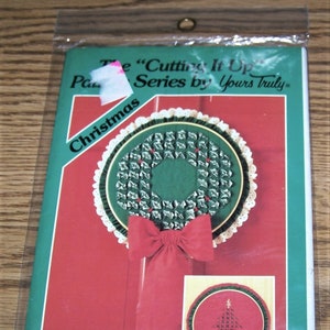 May include: A package containing two Christmas craft patterns from the "Cutting It Up Series by Yours Truly". The patterns feature a wreath and a Christmas tree. The patterns are for hoop wallhanging or vest in 3 sizes.