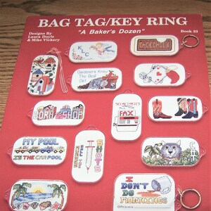 May include: A book cover with a red background and a variety of colorful cross-stitch designs for keychains. The book title is "Bag Tag/Key Ring" and the subtitle is "A Baker's Dozen". The book is designed for 18 count Aida cloth.