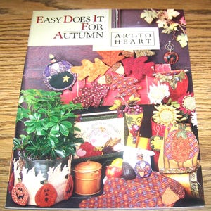 May include: A colorful book cover titled "Easy Does It For Autumn" with various fall-themed crafts. The image features a potted plant, decorative pumpkins, and fabric leaves. The Art to Heart logo is also visible.