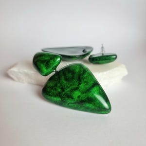May include: A pair of drop earrings featuring two connected, irregular triangular shapes in a glossy, marbled emerald green finish. The earrings have a smooth, polished surface with dark green veining throughout and include silver-toned earring posts.