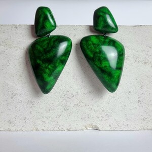 May include: A pair of drop earrings featuring two distinct pieces each, with a smooth, polished finish. The earrings display a vibrant emerald green color with dark, marbled, vein-like patterns throughout the surface of the geometric shapes.