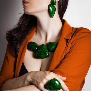 May include: A jewelry set consisting of a statement necklace, drop earrings, and a large ring. Each piece features smooth, polished, dark green marbled resin elements with irregular, rounded, and triangular shapes that have a glossy finish.