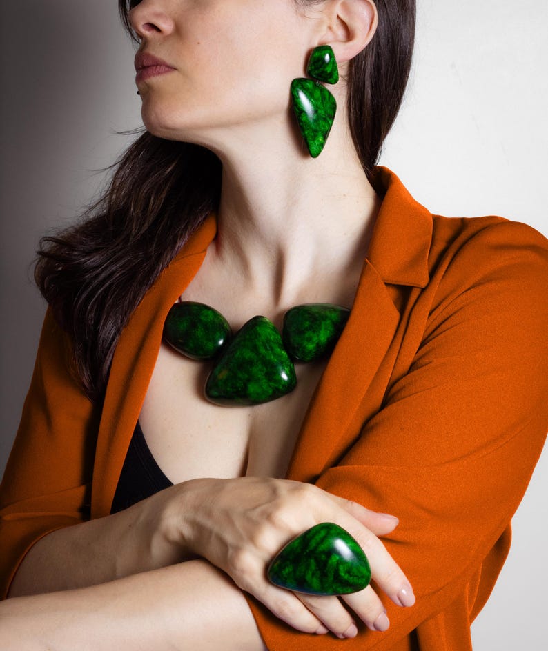 May include: A jewelry set consisting of a statement necklace, drop earrings, and a large ring. Each piece features smooth, polished, dark green marbled resin elements with irregular, rounded, and triangular shapes that have a glossy finish.