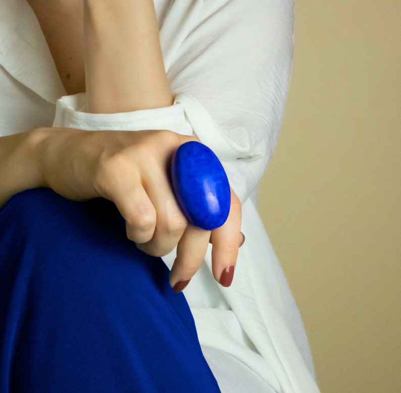 以下が含まれることがあります： 明るい青色の石が付いた大きな楕円形の指輪。指輪は人差し指につけられています。
