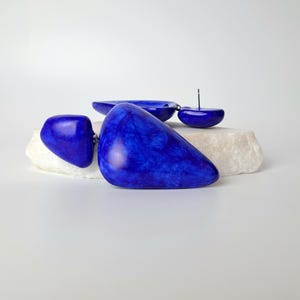 May include: A pair of cobalt blue earrings featuring smooth, irregular, pebble-like shapes with a marbled texture. The earrings are constructed with a post-back closure and consist of two distinct, rounded components linked together in a drop style.