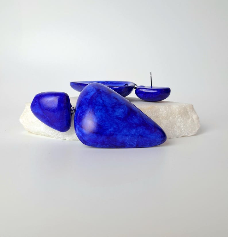 May include: A pair of cobalt blue earrings featuring smooth, irregular, pebble-like shapes with a marbled texture. The earrings are constructed with a post-back closure and consist of two distinct, rounded components linked together in a drop style.