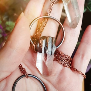 May include: Two crystal pendants on copper chains. One pendant is a clear quartz crystal with a copper wire wrap. The other pendant is a clear quartz crystal with a copper wire wrap and a copper ring.