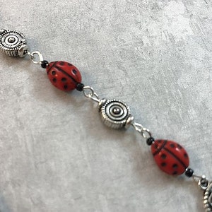 May include: A silver and red ladybug charm bracelet with black beads and silver spacers. The bracelet features a silver charm with a leaf design.