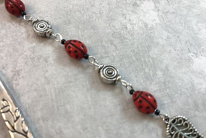 May include: A silver and red ladybug charm bracelet with black beads and silver spacers. The bracelet features a silver charm with a leaf design.