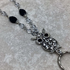 May include: A silver owl charm with clear and black rhinestones, attached to a black and clear beaded lanyard with a silver ring.