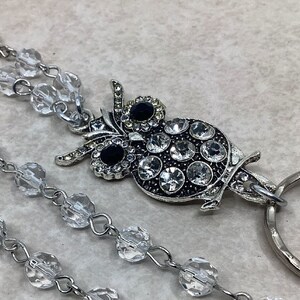 May include: A silver owl charm with clear and black rhinestones hangs from a clear crystal beaded chain with a silver ring attached.