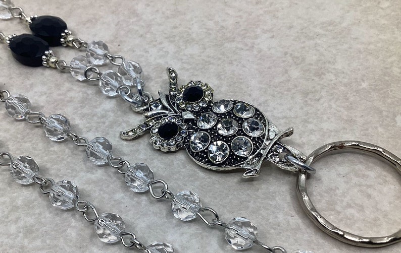 May include: A silver owl charm with clear and black rhinestones hangs from a clear crystal beaded chain with a silver ring attached.