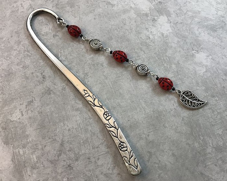 May include: Silver bookmark with a floral design and a chain of red ladybug beads and a silver leaf charm.