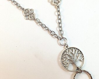 May include: A silver chain necklace with a tree of life pendant and two Celtic knot charms. The necklace has a silver ring attached to the pendant.