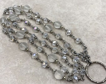 May include: A multi-strand silver chain necklace with clear crystal beads and frosted glass beads. The necklace has a silver clasp with a decorative design and a ring at the end.