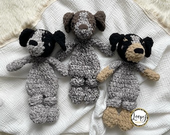 May include: Three crocheted dog plushies in black, brown, and white on a white crocheted blanket with a white fringe. The blanket has a small tag that says "Loopy Couture".