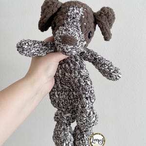 May include: A brown and white crocheted dog plush toy with a brown nose and black eyes. The toy is made with a textured yarn and has a loopy couture label on the bottom.