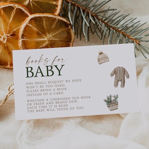 May include: A baby shower invitation card with the text "books for BABY". The card features illustrations of a hat, onesie, and a potted plant. Dried orange slices and greenery are arranged around the card.
