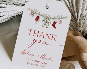 Puede incluir: Una etiqueta de regalo blanca con una cuerda, con las palabras "Thank You" en escritura roja. La etiqueta está decorada con una guirnalda de ropa y adornos navideños para bebés. La etiqueta también incluye el texto "Melissa & Mark's Baby Shower December 12th."