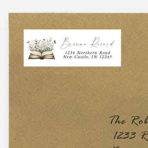 May include: A kraft paper envelope with a white label featuring the name "Brenne Ricard" and address details. The label includes an illustration of an open book with flowers and butterflies. The envelope also has a recipient's address.