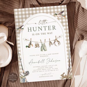 May include: A baby shower invitation with a gingham background and the text "A Little Hunter Is On The Way." The invitation features illustrations of ducks, overalls, and hunting gear. A brown onesie and baby booties are also in the image.